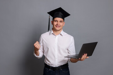 Happy student with laptop after graduation on grey background
