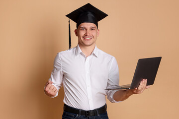 Happy student with laptop after graduation on beige background