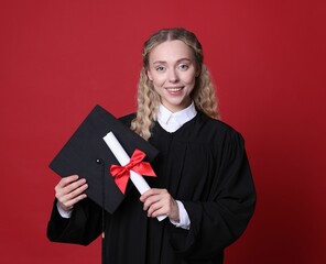 Happy student with diploma and mortarboard after graduation on red background