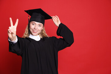Happy student after graduation showing peace sign on red background. Space for text