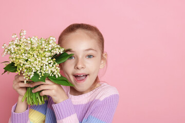 Girl with bouquet of beautiful lily-of-the-valley flowers on light pink background. Space for text
