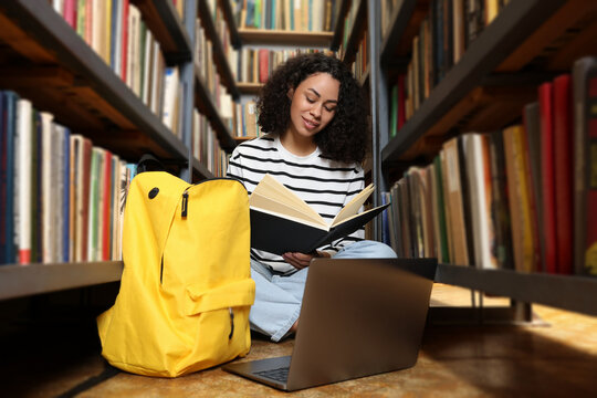 Woman with book studying near shelves in public library - Powered by Adobe
