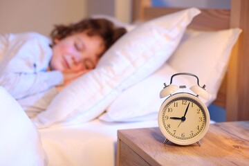 Little boy sleeping in bed at home, focus on alarm clock