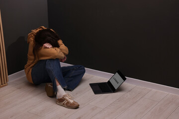 Cyber bullying. Upset teenage girl and laptop with text You Loser on floor indoors. Space for text