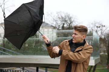 Man with broken umbrella fighting wind under rain outdoors © New Africa