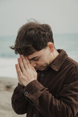 Religious Boy Praying God At The Sea On His Knees During Overcast Day