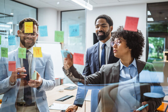 Coworkers brainstorming and planning use sticky notes on glass wall