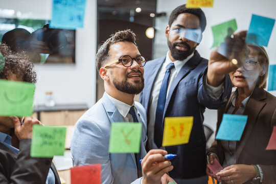 Coworkers brainstorming and planning use sticky notes on glass wall