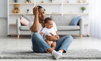 Daddy Blues. Stressed Young Black Father Sitting With Crying Infant Baby On Floor At Home,...