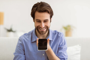 Voice Assistant App. Cheerful Man Using Smartphone With Voice Search Application Sitting On Couch At Home. Guy Chatting On Cellphone Using Loudspeaker Mode. Modern Gadgets Lifestyle Concept.