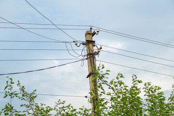 A utility pole stands tall amidst lush green foliage, supporting several power lines. The overcast...
