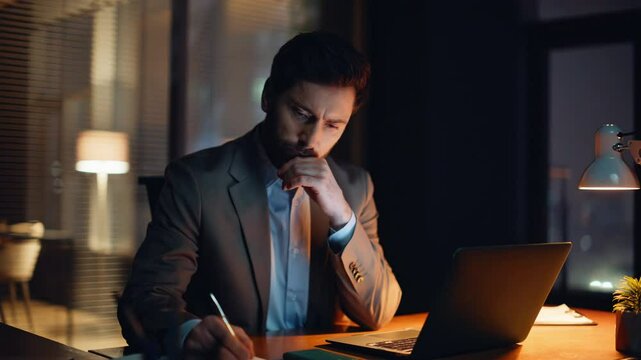 Serious businessman browsing computer writing notes at cozy dark flat closeup