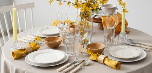 Elegant table setting with clean plates, burning candles, cutlery and blooming tree branches