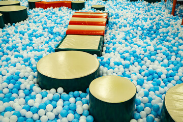 A vibrant indoor play space features a large ball pit filled with blue and white balls.