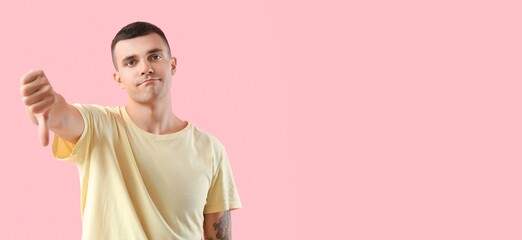 Young man showing dislike on pink background with space for text