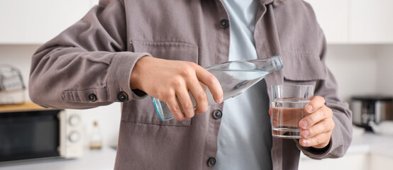 Young man with pouring water in glass at home, closeup