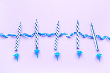 Blue birthday candles and ribbon on lilac background