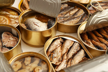 Many opened cans with different fish on tiled table, closeup