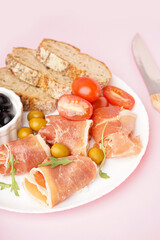 Plate with slices of tasty jamon with bread on pink background, closeup