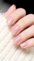 Photo of Elegant pink manicure with glitter on a woman's hand against a soft white knitted background