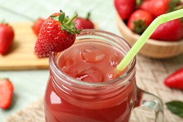 Mason jar of juice and bowl with strawberry on green wooden table
