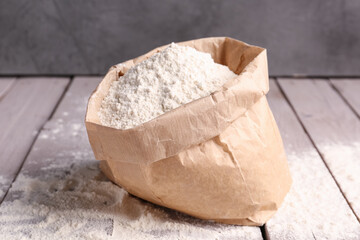 Paper bag with wheat flour on grey wooden table near wall