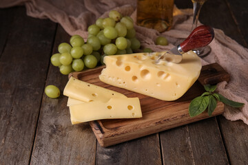 Board with tasty Swiss cheese and grapes on wooden background