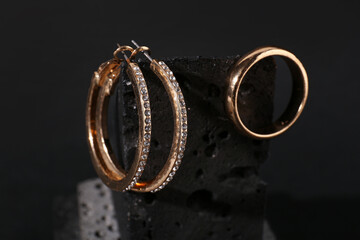 Decorative podium with beautiful ring and earrings on black background