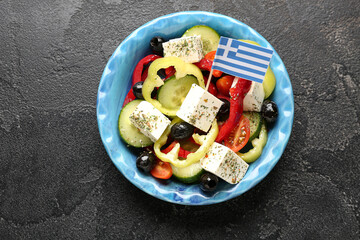 Bowl of salad with feta cheese, olives and Greek flag on black grunge table