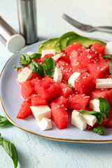 Plate of tasty watermelon salad on light blue background