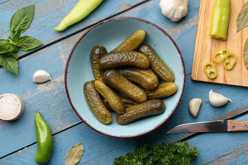 Bowl with pickled cucumbers and different spices on blue wooden background
