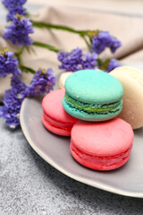 Plate with sweet macaroons and beautiful flowers on grey background