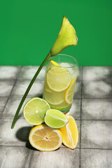 Glass of tasty cocktail with lime and lemon pieces on grunge tile near green wall