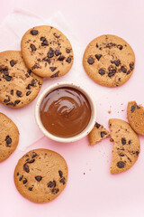 Tasty cookies with chocolate chips and bowl of sauce on pink background