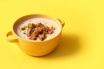 Pot of tasty cream soup with croutons on yellow background
