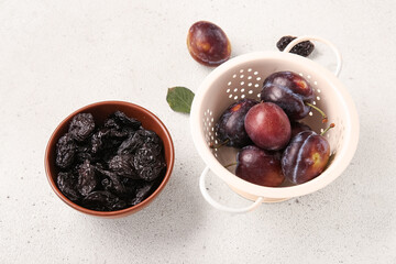 Bowl with tasty dried plums and colander of fresh fruits on white background