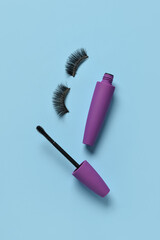 Black mascara in purple tube and fake eyelashes on blue background