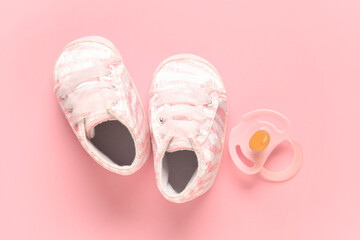 Stylish baby shoes with pacifier on pink background