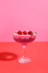 Glass of Cosmopolitan cocktail with cherries on colorful background