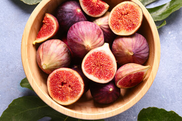 Bowl with ripe fresh figs and plant leaves on grunge blue background