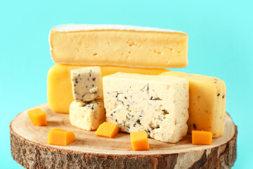 Wooden board with tasty cheese on blue background