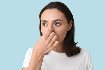 Young woman touching her nose on blue background, closeup