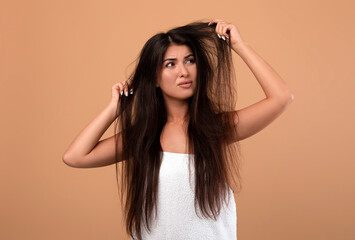 Frustrated armenian woman showing her damaged long locks on beige studio background. Young lady having bad hair day, upset over her messy hairdo. Hairdressing services concept