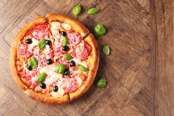 Tasty pizza with salami, cheese, basil and olives on wooden table, flat lay. Space for text