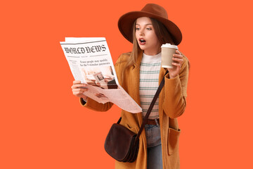 Shocked young woman with newspaper and coffee cup on orange background