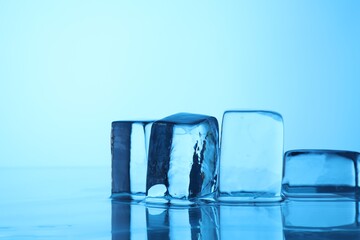 Cubes of clear ice on light blue background, closeup. Space for text