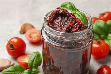 Delicious sun dried tomatoes, fresh vegetables, basil and garlic on light grey table, closeup