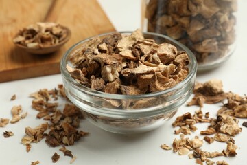 Pieces of dry chicory roots in bowl, jar and spoon on white table, closeup