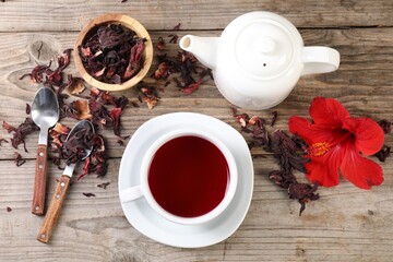 Delicious hibiscus tea in cup, teapot, dry roselle sepals and flower on wooden table, flat lay