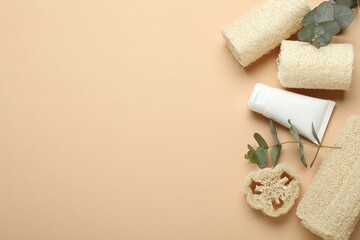 Loofah sponges, cosmetic product and eucalyptus leaves on beige background, flat lay. Space for text